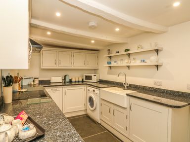 A kitchen with white cabinets a washing machine microwave and shelves with cups at Cousham Cottage in Kingsand And Cawsand