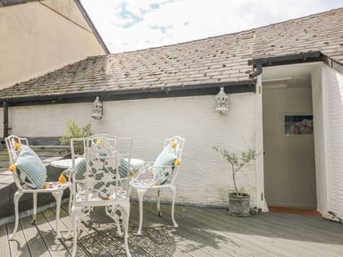 An outdoor patio with white metal chairs and table with cushions on the chairs at Cousham Cottage in Kingsand And Cawsand