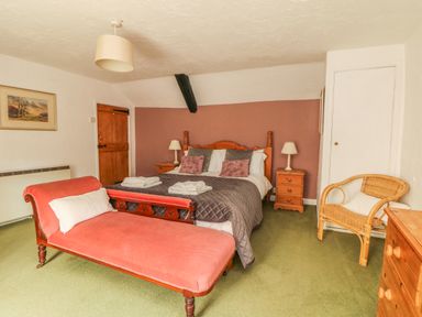 A bedroom with a double bed two bedside tables with lamps a wooden door a wicker chair and a pink chaise lounge at Cousham Cottage in Kingsand And Cawsand