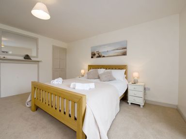 A bedroom with a wooden bed frame bedside tables with lamps a large mirror and a painting on the wall at Nirvana in Kingsand And Cawsand