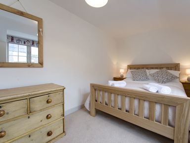 A bedroom with a wooden bed with pillows and rolled towels a wooden chest of drawers and a mirror at Nirvana in Kingsand And Cawsand