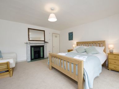 A bedroom with a wooden bed and matching bedside tables next to a fireplace with a mirror above at Nirvana Kingsand And Cawsand