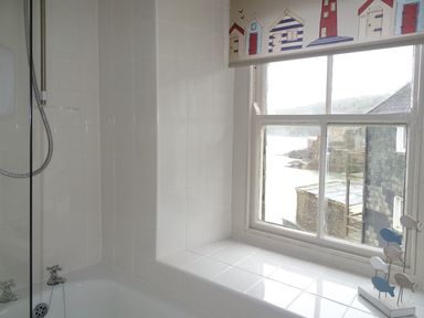 A bathroom with a bathtub and shower next to a window with a decorative blind and a small fish ornament on the sill at Nirvana in Kingsand And Cawsand