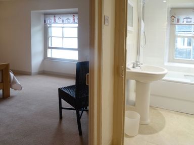 A bedroom with a chair and window beside a bathroom with a sink and bathtub at Nirvana Kingsand And Cawsand