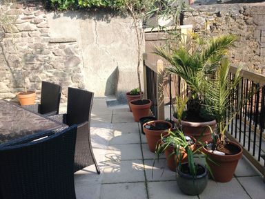An outdoor patio with black woven chairs a glass table and various potted plants along a railing at Nirvana Kingsand And Cawsand