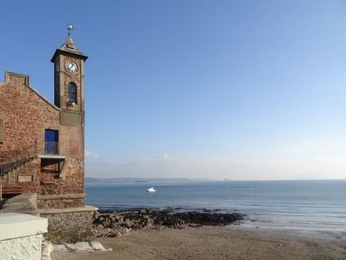 A clock tower next to a rocky beach and ocean with a boat on the water at Nirvana Kingsand And Cawsand