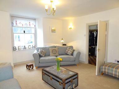 A living room with blue sofas a trunk coffee table and a window with beach letters at Nirvana Kingsand And Cawsand