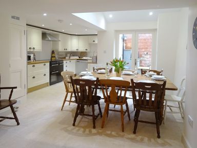A kitchen with a wooden dining table set with plates and glasses and wooden chairs at Nirvana in Kingsand And Cawsand