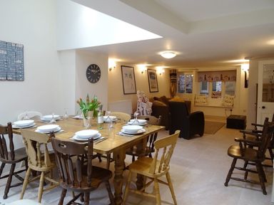 A dining area with a wooden table set for eight and a living room with sofas and windows at Nirvana Kingsand And Cawsand
