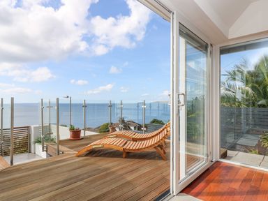 A wooden deck with two lounge chairs and glass railing overlooking the ocean at Rock Rose in Downderry