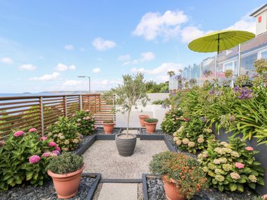 A garden with potted plants and flowers by a wooden fence with a sea view at Rock Rose in Downderry