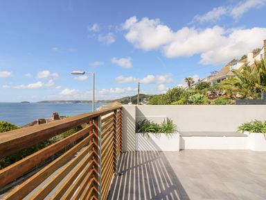 An outdoor terrace with wooden railing planter boxes and a built in bench overlooking the sea at Rock Rose in Downderry