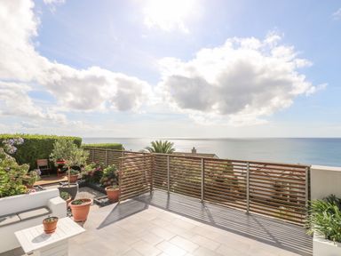A terrace with potted plants and a white sofa overlooking the sea at Rock Rose in Downderry