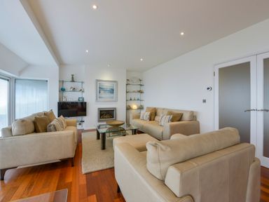 A living room with beige sofas a glass coffee table and shelves with decorations at Rock Rose in Downderry