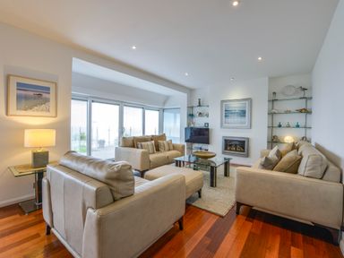 A living room with beige sofas glass coffee table and fireplace at Rock Rose in Downderry