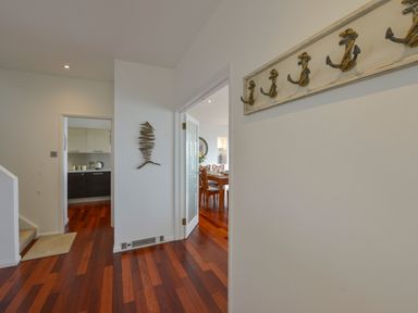 A hallway with wooden floor leading to a kitchen and dining room with wall decorations at Rock Rose in Downderry