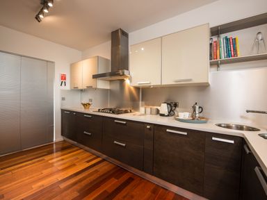 A kitchen with wooden lower cabinets and light upper cabinets a gas stove a kettle and cookbooks on a shelf at Rock Rose in Downderry