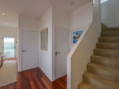 An entryway with carpeted stairs wooden floor two white doors and a mirror on the wall at Rock Rose in Downderry