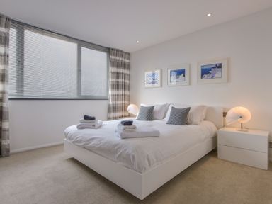 A bedroom with a bed with pillows and towels next to a window with blinds and curtains at Rock Rose in Downderry