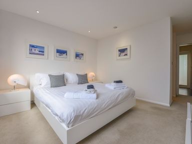 A bedroom with a double bed bedside tables and framed pictures on walls at Rock Rose in Downderry