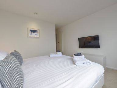 A bedroom with a bed with white sheets and two pillows and a wall-mounted TV at Rock Rose in Downderry