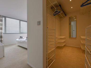 A bedroom with a bed and folded towels next to a walk in closet with shelves and a mirror at Rock Rose in Downderry