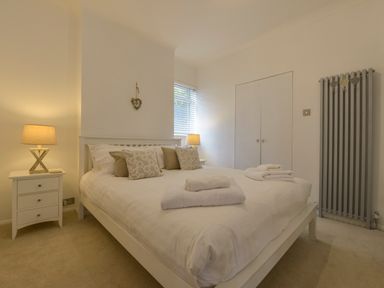 A bedroom with a bed with pillows and towels bedside tables with lamps and a radiator on the wall at Rock Rose in Downderry
