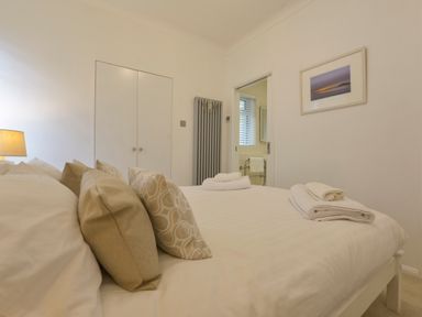 A bedroom with a bed with pillows and folded towels a closed door a radiator and a framed picture on the wall at Rock Rose in Downderry
