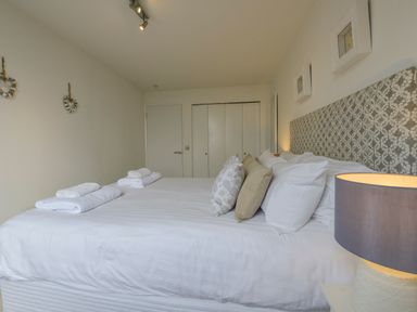 A bedroom with a large bed with pillows and towels bedside lamp and wall decorations at Rock Rose in Downderry