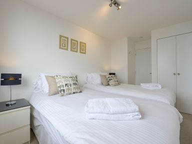 A bedroom with two single beds white linens bedside table with lamp and framed pictures above the beds at Rock Rose in Downderry