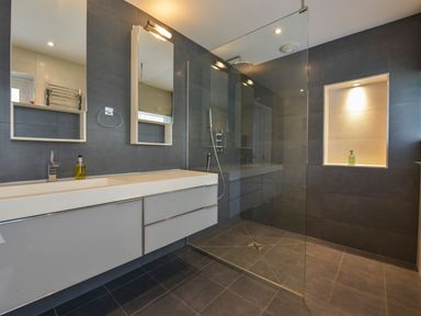 A modern bathroom with a double sink vanity a large mirror and a walk in shower at Rock Rose in Downderry