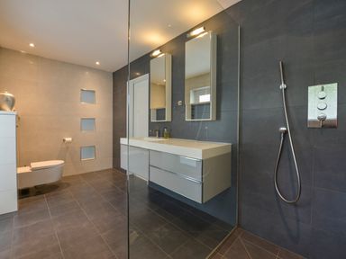 A modern bathroom with a wall-mounted toilet a double sink vanity and a walk-in shower at Rock Rose in Downderry
