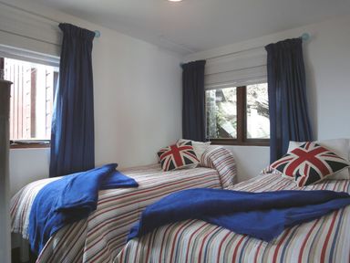 A bedroom with two single beds with striped bedding and blue blankets at Seagulls Nest Whitsand Bay near Millbrook