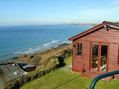 A wooden cabin on a grassy hill overlooking the ocean with waves near Seagulls Nest in Whitsand Bay near Millbrook