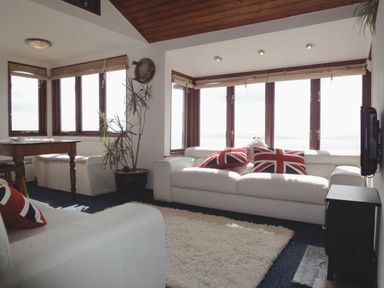 A living room with white sofas and Union Jack cushions and a wooden dining table at Seagulls Nest in Whitsand Bay near Millbrook