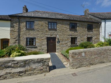 A stone cottage with six windows and a dark wooden door with plants along the front at Samuels Cottage in Lanreath