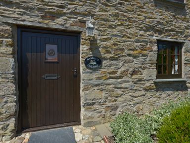 A stone wall with a dark wooden door and window with plants below at Samuels Cottage in Lanreath