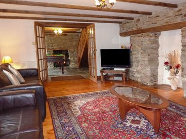 A living room with a leather sofa a glass coffee table a television and an adjoining room with a pool table at Samuels Cottage in Lanreath