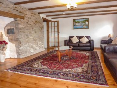 A living room with leather sofas a wooden coffee table a patterned rug a stone wall and a painting at Samuels Cottage in Lanreath