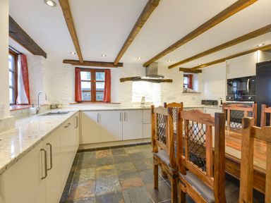 A kitchen with wooden chairs and a table slate tile flooring and wooden ceiling beams at Samuels Cottage in Lanreath