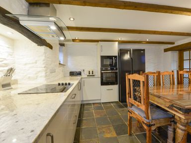 A kitchen with wooden dining chairs a wooden dining table black refrigerator and built in oven at Samuels Cottage in Lanreath
