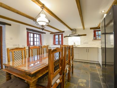 A kitchen with a large wooden dining table and chairs stone tile flooring and wooden ceiling beams at Samuels Cottage in Lanreath