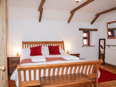 A bedroom with wooden bed frame red pillows bedside tables lamps and a small window at Samuels Cottage in Lanreath