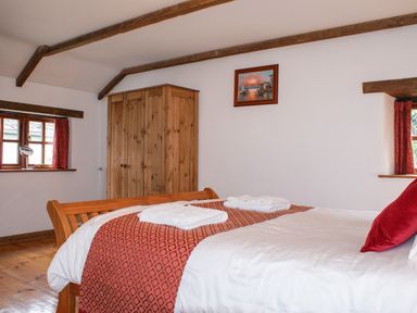 A bedroom with a wooden bed with white and red bedding a wooden wardrobe and two windows at Samuels Cottage in Lanreath