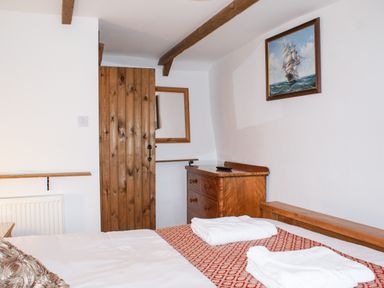 A bedroom with a wooden door wooden dresser folded towels on bed and a painting of a ship on the wall at Samuels Cottage in Lanreath