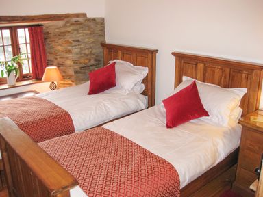 A bedroom with two single wooden beds with white bedding and red cushions at Samuels Cottage in Lanreath