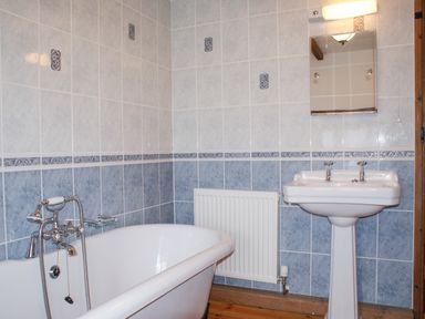 A bathroom with a bathtub a sink a mirror and a radiator at Samuels Cottage in Lanreath