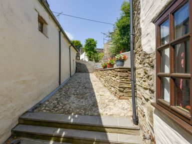 A narrow outdoor stone pathway with stone steps and flower pots near walls at Samuels Cottage in Lanreath