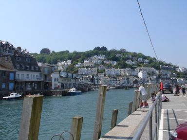 A harbor with boats moored near buildings and houses on a hillside at Samuels Cottage in Lanreath