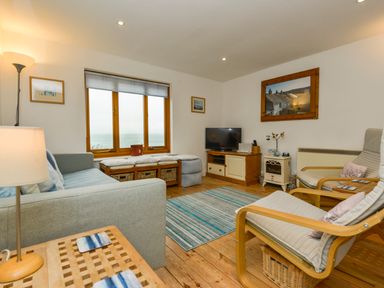 A living room with a sofa chairs a television and a window with a sea view at Chough Cottage in Kingsand And Cawsand